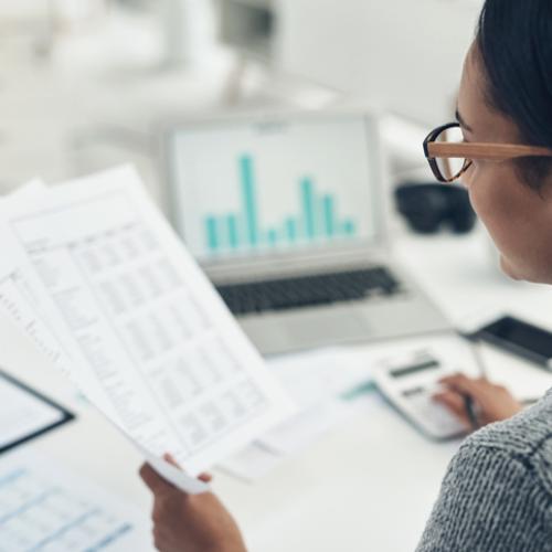 photo of a lady holding business paperwork with a laptop in the background